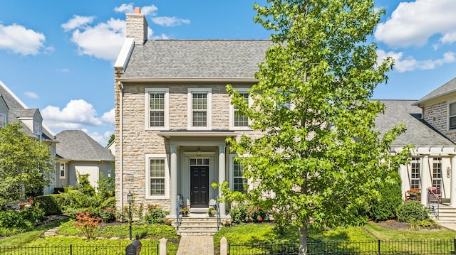 view of front of house featuring a chimney, a shingled roof, a fenced front yard, and stone siding