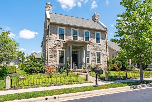 view of front facade featuring a shingled roof, a chimney, a fenced front yard, and stone siding