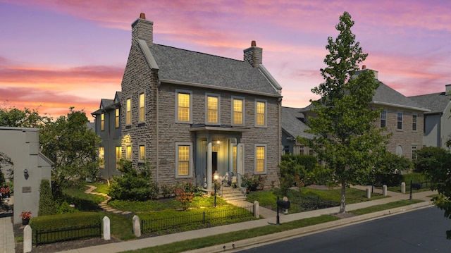 view of front of house featuring a shingled roof, stone siding, and a fenced front yard