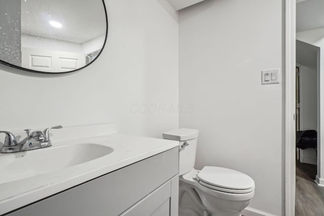 half bathroom with vanity, baseboards, toilet, and wood finished floors