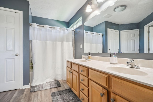 full bathroom featuring a sink, double vanity, wood finished floors, and a textured ceiling