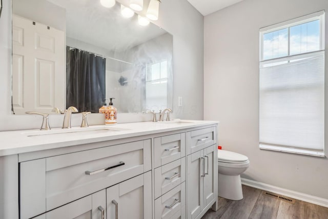 full bath featuring a shower with shower curtain, toilet, visible vents, a sink, and wood finished floors