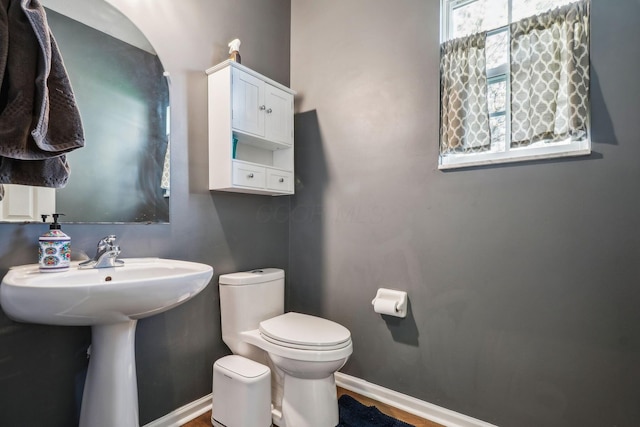 half bathroom with toilet, a sink, and baseboards