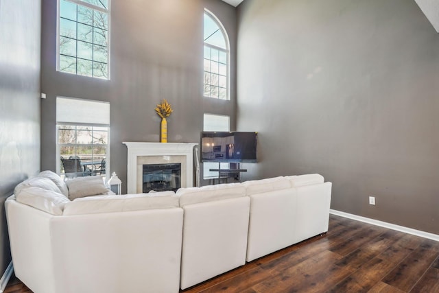 living room featuring a glass covered fireplace, dark wood-type flooring, a high ceiling, and baseboards