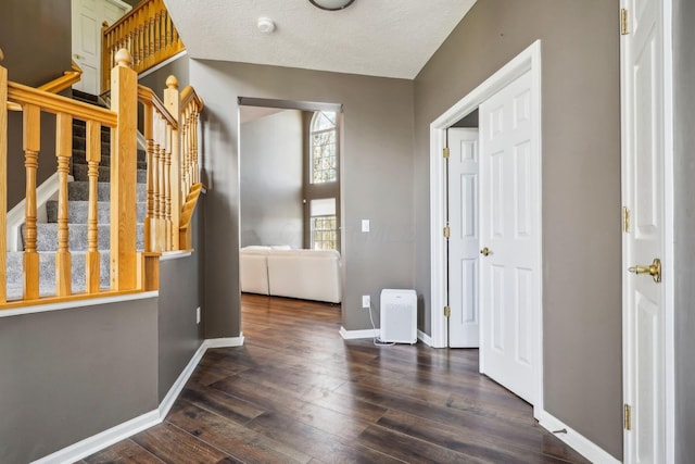 corridor with stairway, baseboards, a textured ceiling, and wood finished floors