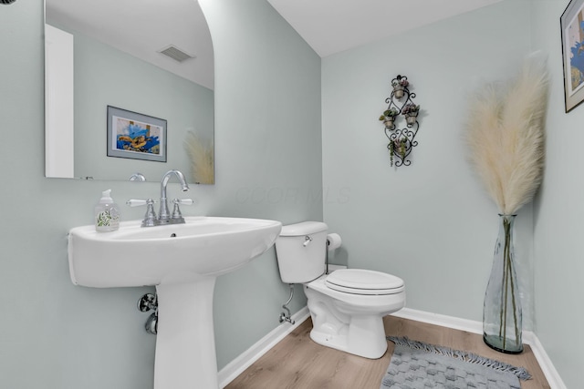 half bath with baseboards, toilet, visible vents, a sink, and wood finished floors