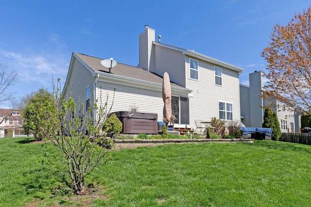 back of house featuring a chimney, a hot tub, and a lawn