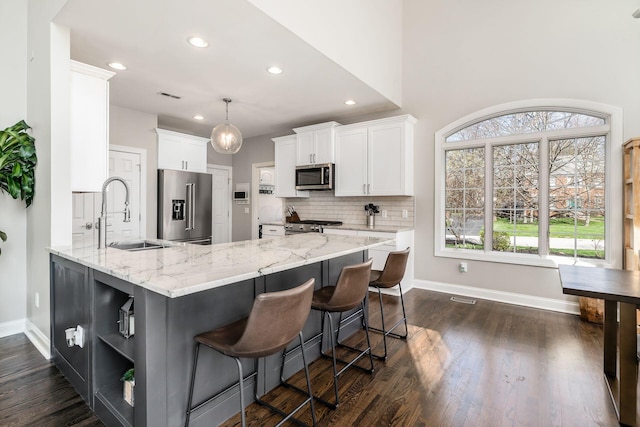 kitchen with a peninsula, light stone countertops, decorative backsplash, stainless steel appliances, and a sink