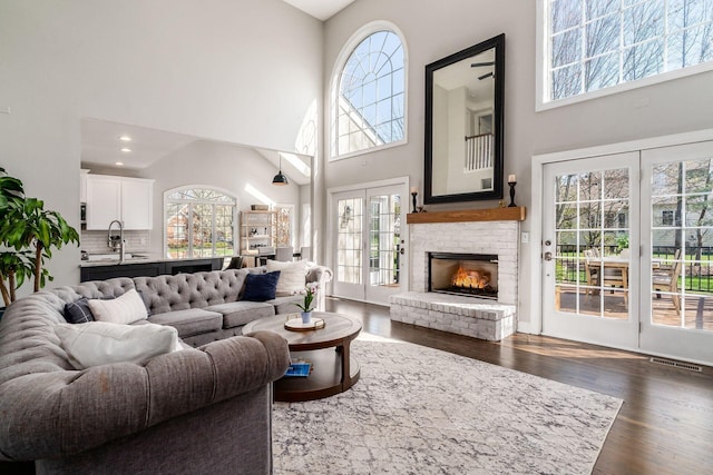 living room featuring a towering ceiling, dark wood-style floors, and a brick fireplace