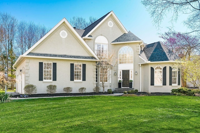french country style house featuring roof with shingles, a front lawn, and stucco siding