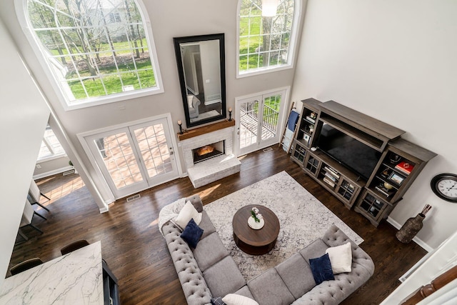 living room with visible vents, baseboards, a high ceiling, a warm lit fireplace, and dark wood-type flooring
