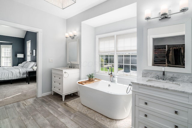 full bathroom featuring two vanities, a soaking tub, a sink, and wood finished floors