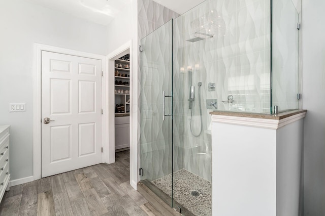 bathroom featuring a spacious closet, a stall shower, and wood finished floors