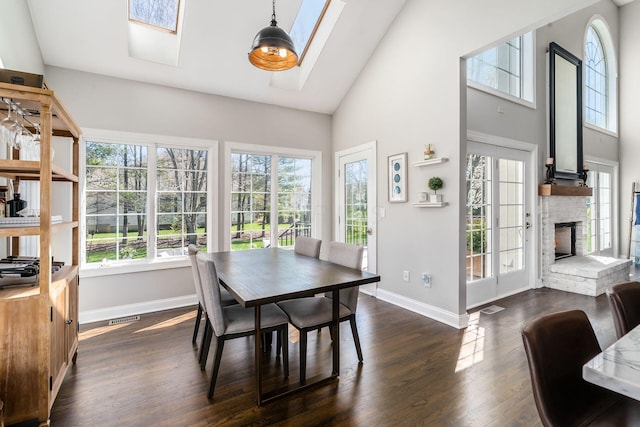dining room featuring dark wood finished floors, a stone fireplace, visible vents, a skylight, and baseboards