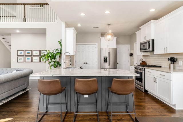 kitchen with white cabinets, a sink, open floor plan, high quality appliances, and dark wood-type flooring