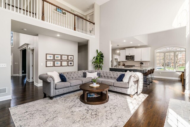 living area featuring a towering ceiling, ornamental molding, visible vents, dark wood-style flooring, and baseboards