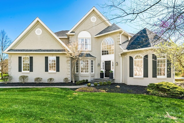view of front of property featuring roof with shingles, stucco siding, and a front lawn