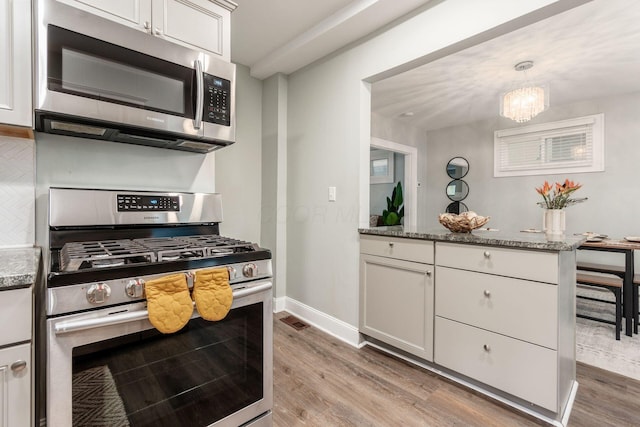 1069 Miller Ave, Columbus, OH 43206 - kitchen with stainless steel appliances, light wood finished floors, a peninsula, stone counters, and a chandelier