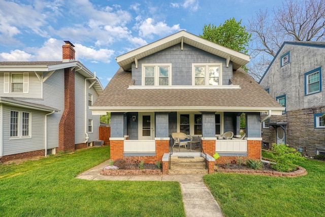 view of front of house with a shingled roof, a porch, and a front lawn