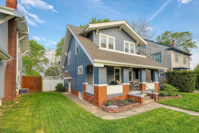 view of front facade featuring a front lawn, fence, covered porch, a shingled roof, and a gate