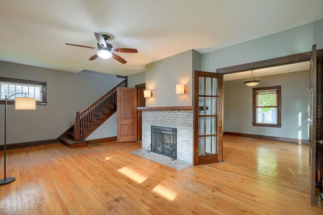unfurnished living room featuring stairs, a fireplace, baseboards, ceiling fan, and light wood-type flooring