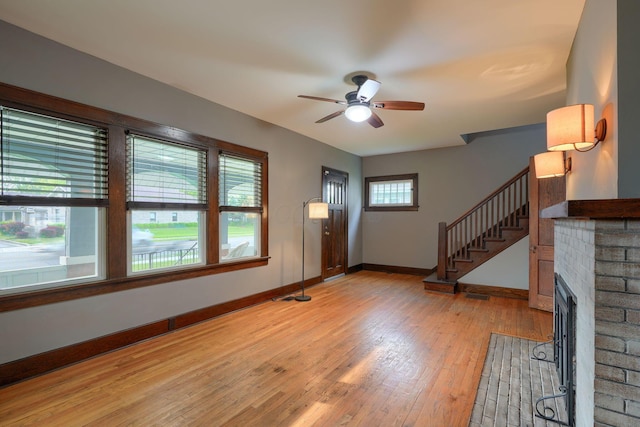 unfurnished living room featuring light wood finished floors, a fireplace, stairs, a ceiling fan, and baseboards