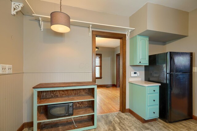 kitchen with wainscoting, light countertops, light wood finished floors, black appliances, and blue cabinetry