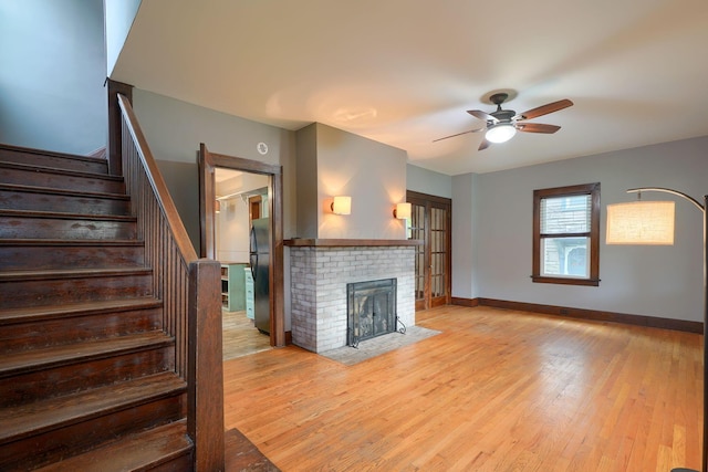 unfurnished living room with baseboards, a ceiling fan, light wood finished floors, and stairway