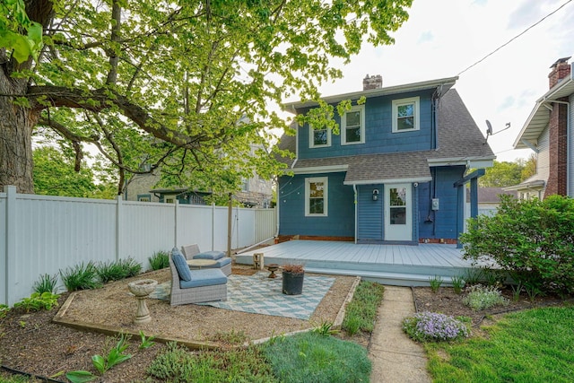 back of property featuring a fenced backyard, a wooden deck, a chimney, and roof with shingles