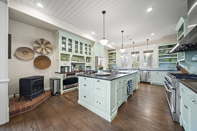 kitchen featuring wall chimney range hood, open shelves, a sink, dark countertops, and stainless steel appliances