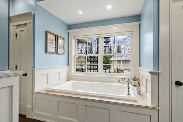bathroom with a garden tub, recessed lighting, a decorative wall, and a wainscoted wall