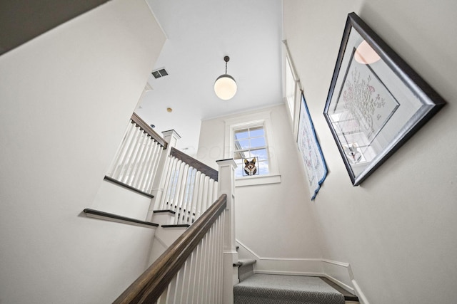 staircase featuring visible vents, a high ceiling, and baseboards