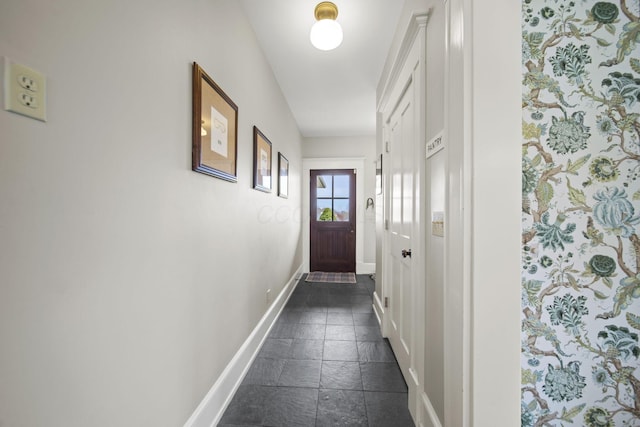 doorway with baseboards and stone tile flooring