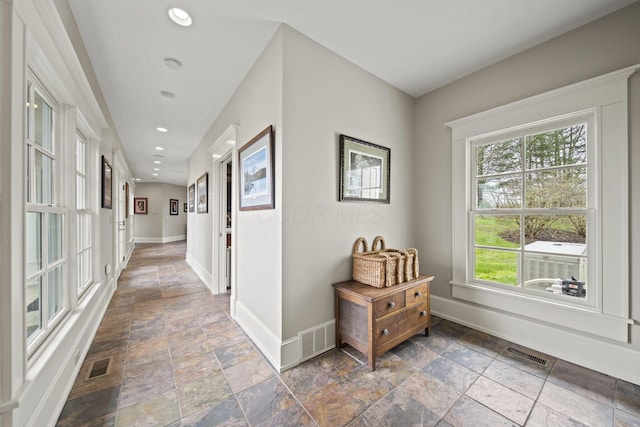 hall with visible vents, baseboards, and stone tile floors
