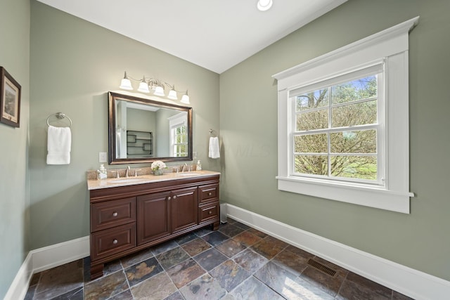 full bathroom featuring a healthy amount of sunlight, a sink, baseboards, and stone tile floors