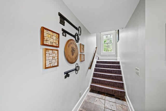 stairway featuring baseboards and stone tile flooring