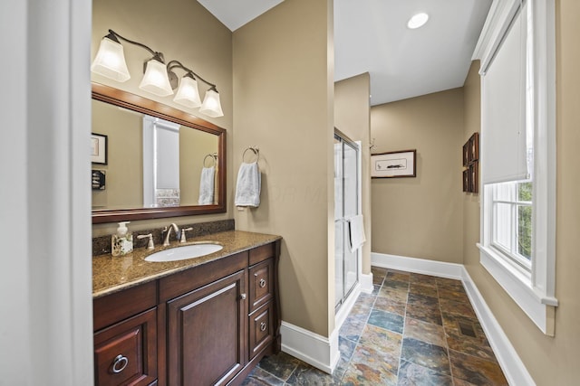 full bathroom featuring baseboards, a stall shower, stone tile floors, and vanity