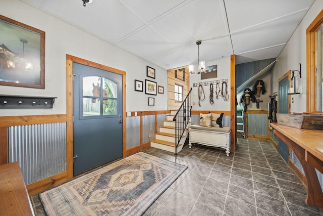 entryway featuring stairs, wooden walls, an inviting chandelier, and a wainscoted wall