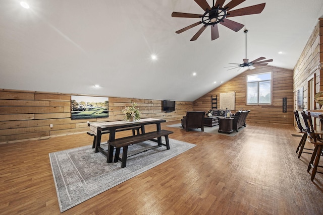 playroom with ceiling fan, a wood stove, vaulted ceiling, wood finished floors, and wooden walls