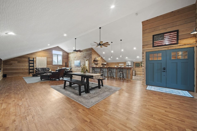 dining space with wood walls, ceiling fan, light wood-type flooring, and high vaulted ceiling