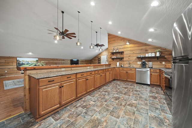 kitchen featuring a ceiling fan, appliances with stainless steel finishes, light stone counters, lofted ceiling, and wooden walls