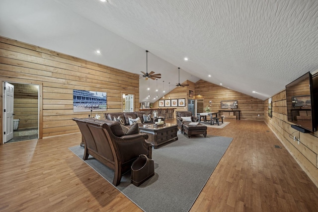 living room with vaulted ceiling, a textured ceiling, a ceiling fan, wood walls, and light wood finished floors