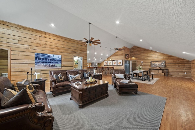 living area with ceiling fan, a textured ceiling, wood finished floors, vaulted ceiling, and wood walls