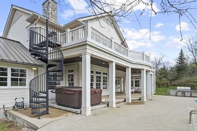 rear view of house featuring exterior kitchen, a patio, stairway, a hot tub, and a standing seam roof