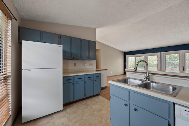kitchen with a sink, a textured ceiling, vaulted ceiling, white appliances, and blue cabinetry