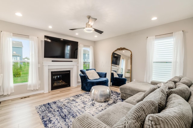living area featuring ceiling fan, a wealth of natural light, light wood-style floors, and a fireplace