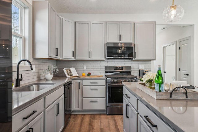kitchen featuring decorative light fixtures, a sink, dark wood-style flooring, appliances with stainless steel finishes, and backsplash