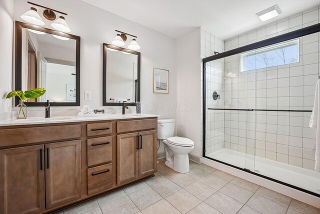 bathroom featuring a sink, toilet, a shower stall, double vanity, and tile patterned floors