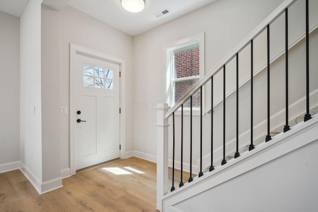 foyer with baseboards, wood finished floors, visible vents, and stairway