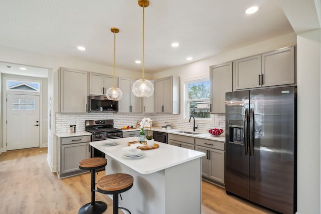 kitchen featuring a sink, decorative backsplash, light wood finished floors, appliances with stainless steel finishes, and gray cabinetry